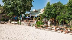 A beachside resort with a sandy walkway, wooden fences, and umbrellas.