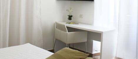 A bedroom with a bed, a desk, and a TV.