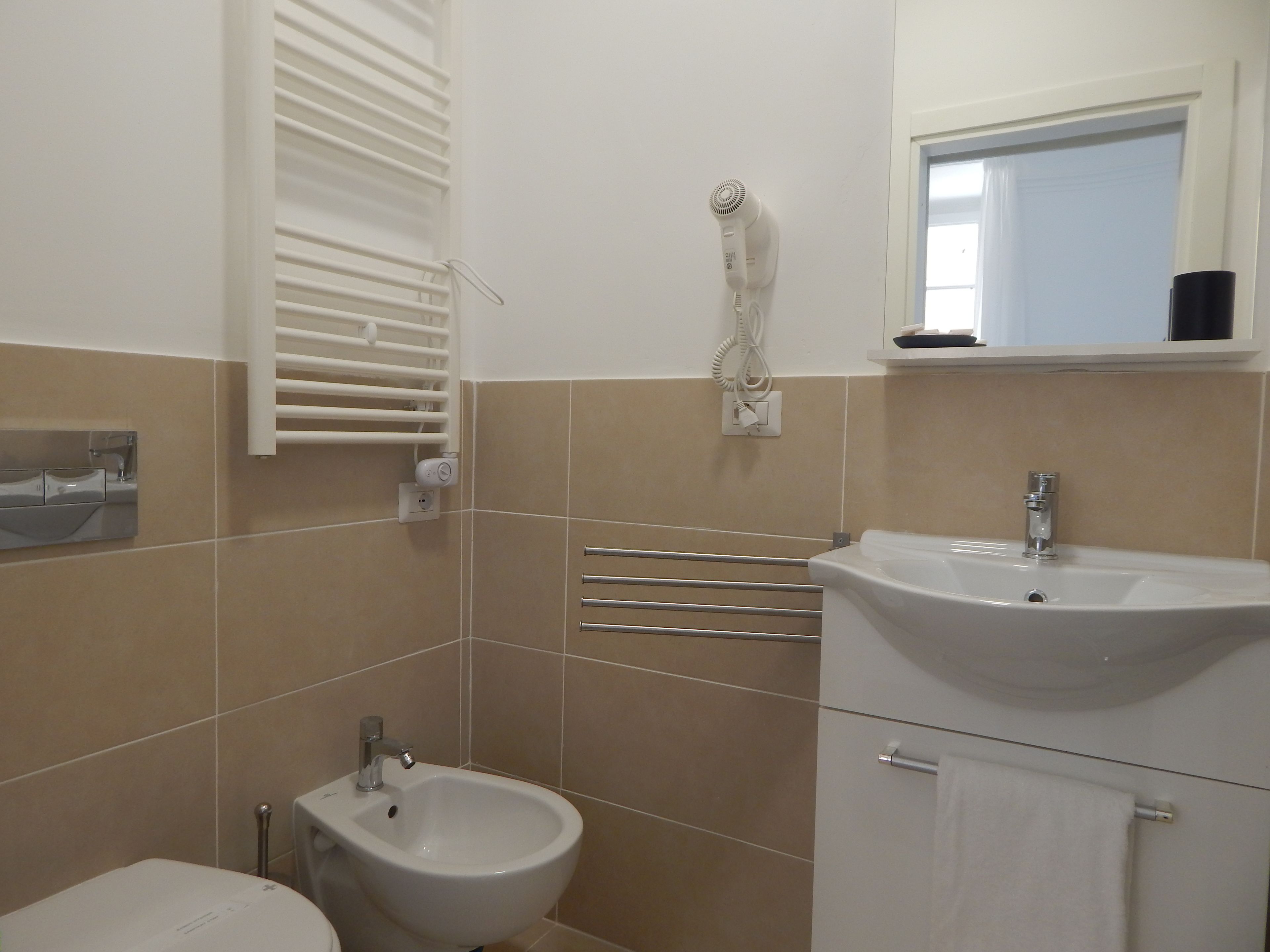 A bathroom with a bidet, a sink, a mirror, and a towel rack.