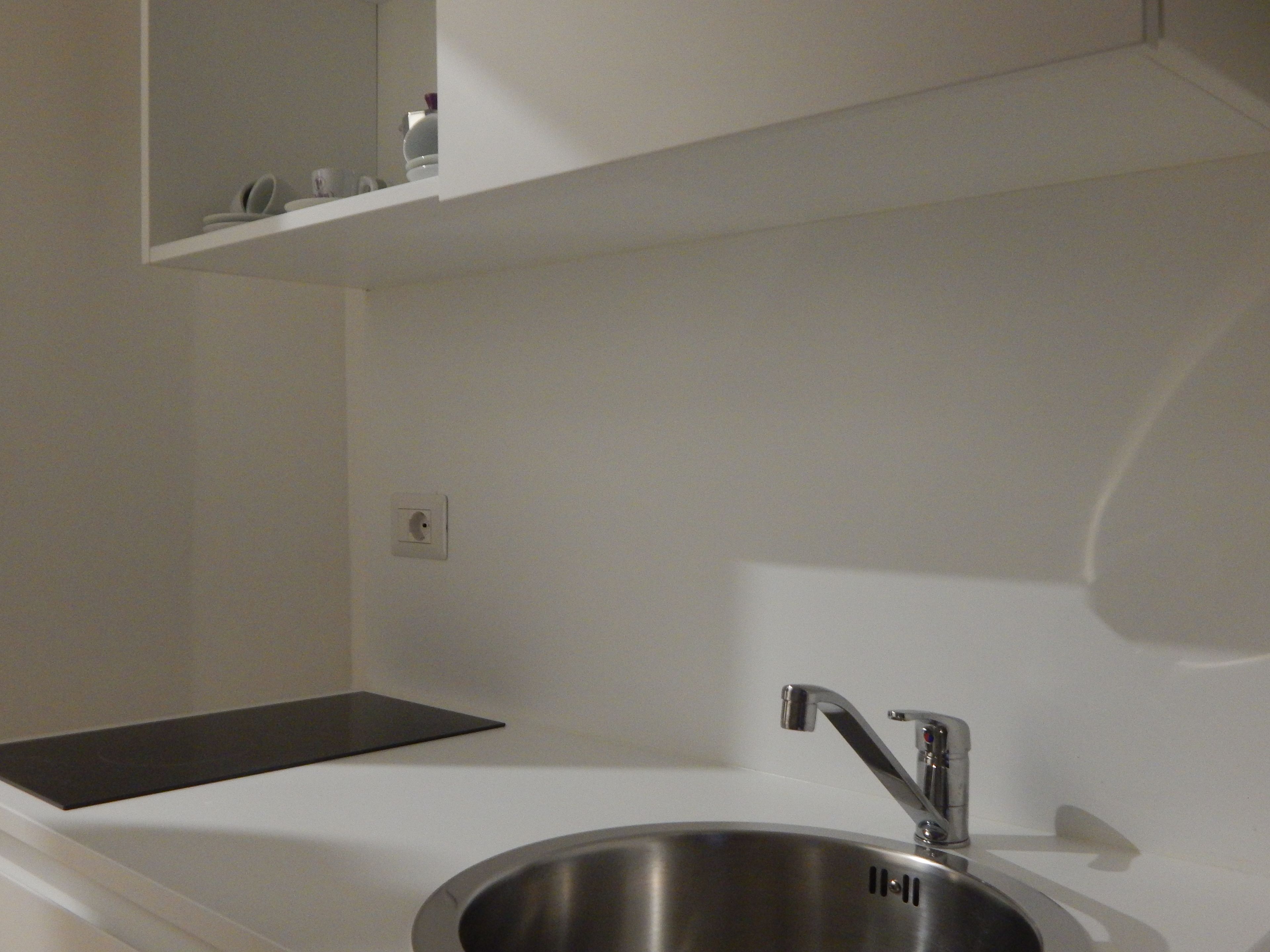A stainless steel kitchen sink with a modern faucet, a white countertop, and a small shelf above the sink.