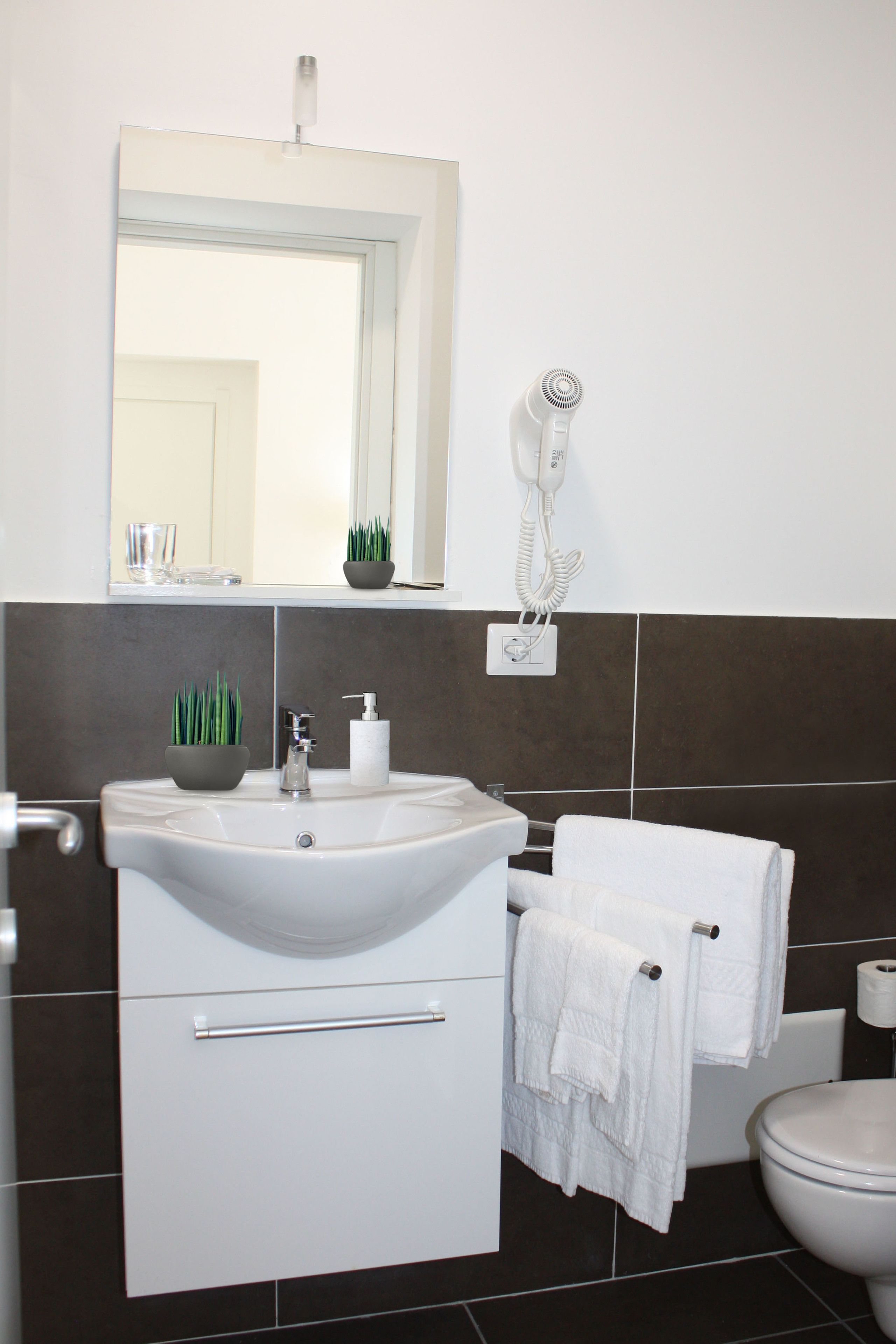 A bathroom with a white sink, a mirror, a hairdryer, and a toilet.