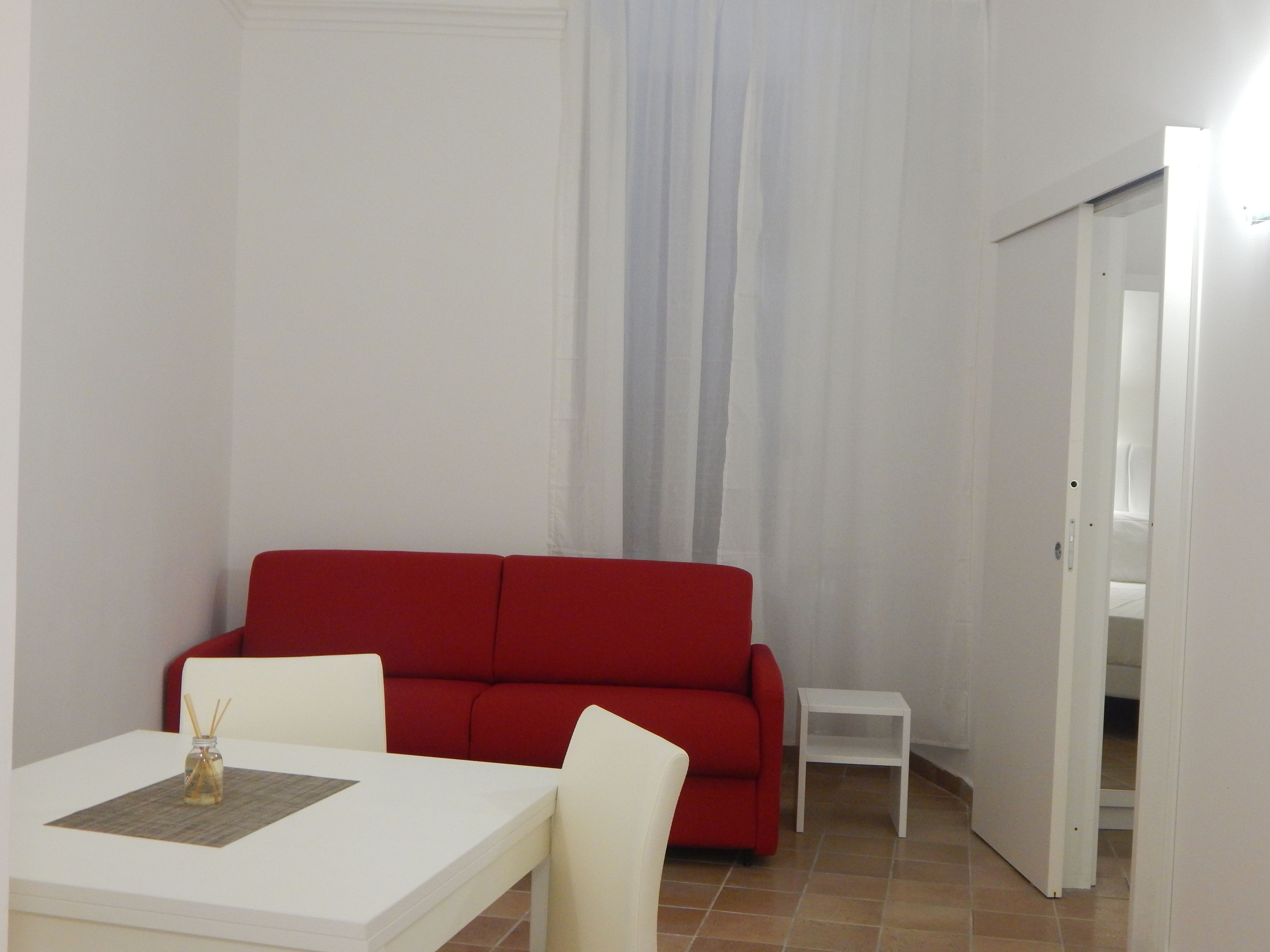 A room with a white table, red sofa, and a small white side table.