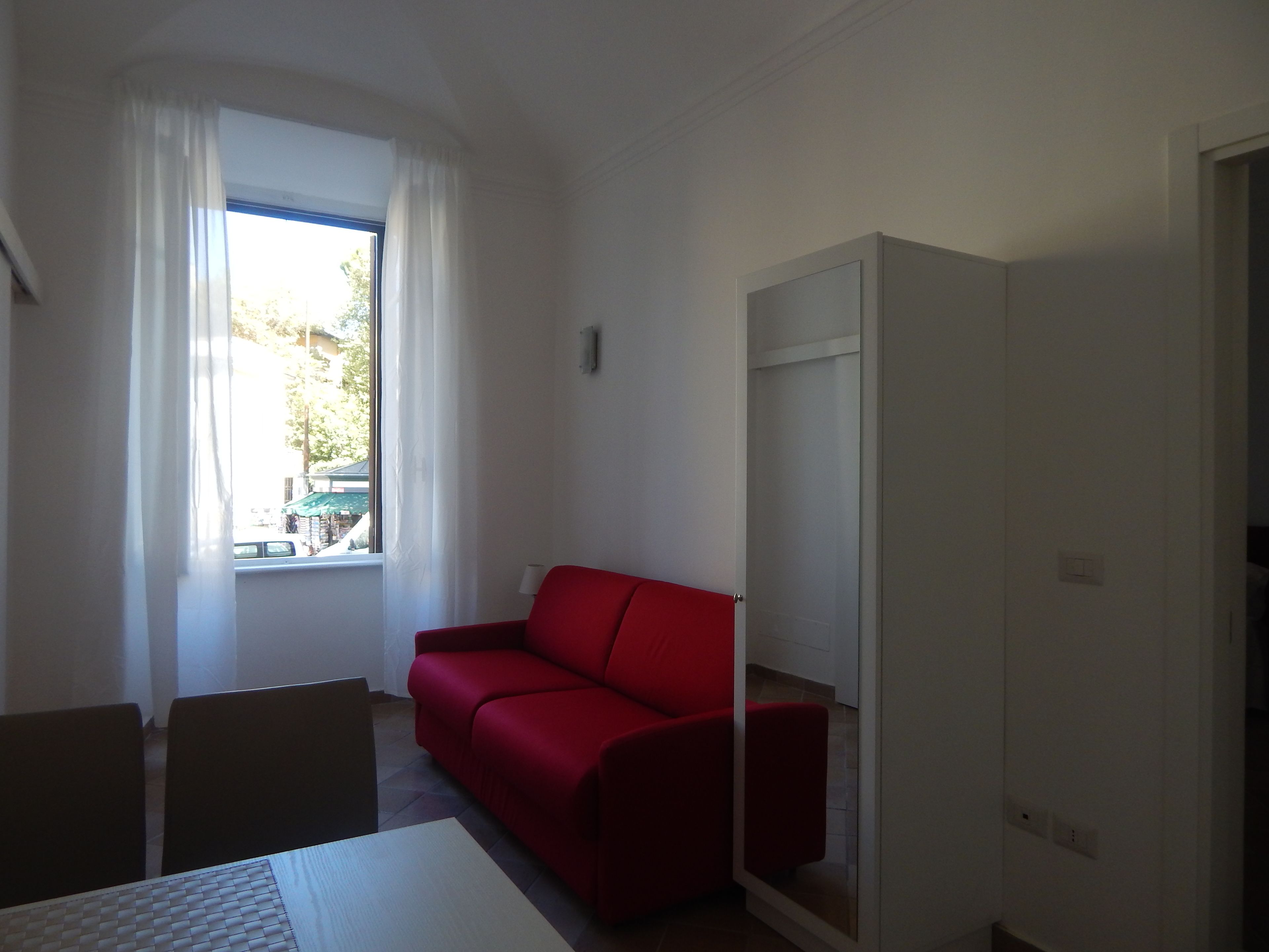 Een kamer met een rode bank, een witte kast en een raam met gordijnen.