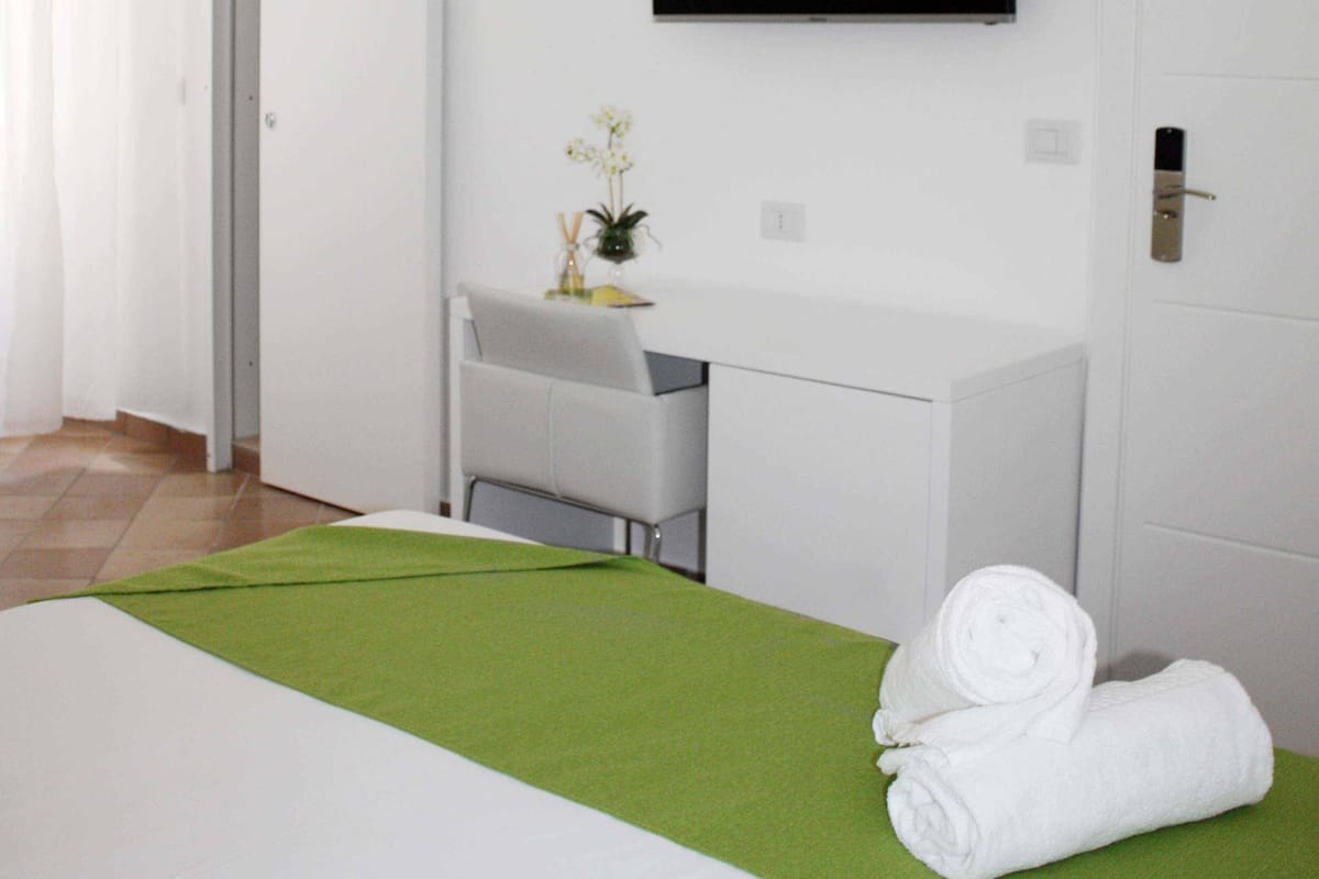 Ein Hotelzimmer mit Bett, Schreibtisch, Stuhl, einem an der Wand befestigten Fernseher und einer Klimaanlage.