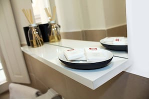 A bathroom counter with a white sink, a black tray with soap, and two glass jars with reed diffusers. - Roma Resort Colosseum (Rome)