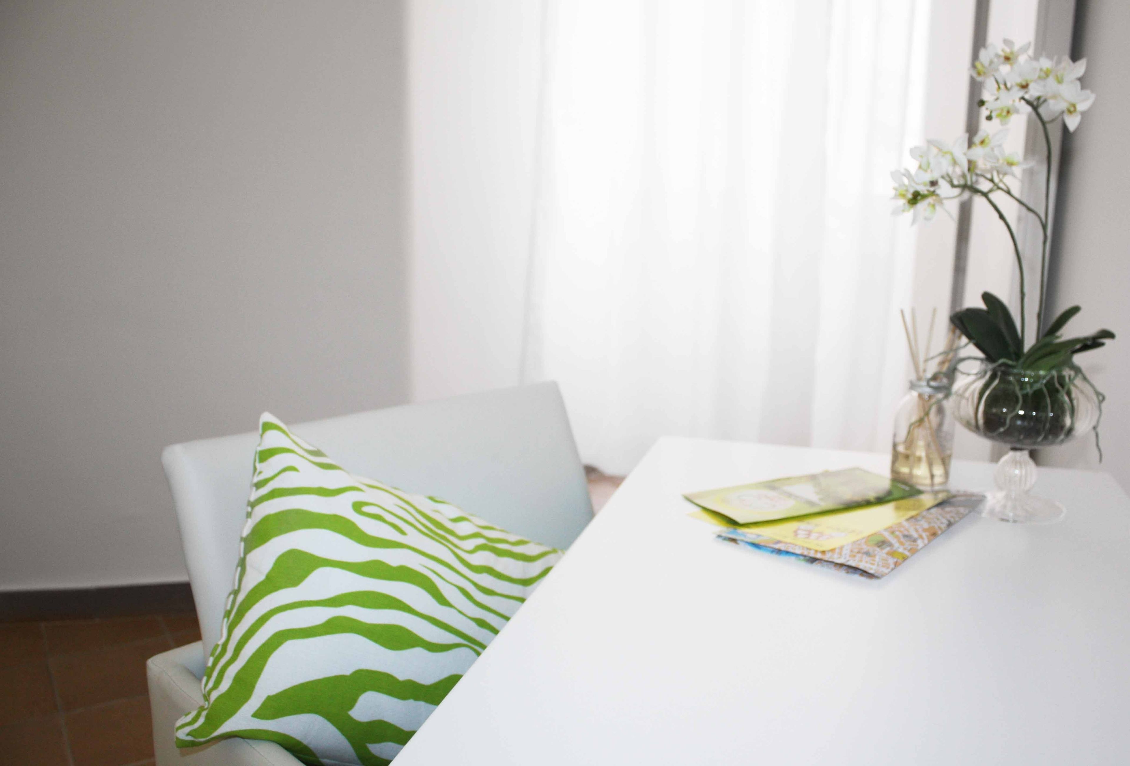 A white dining table with a zebra-patterned pillow, a vase with white flowers, and a book.
