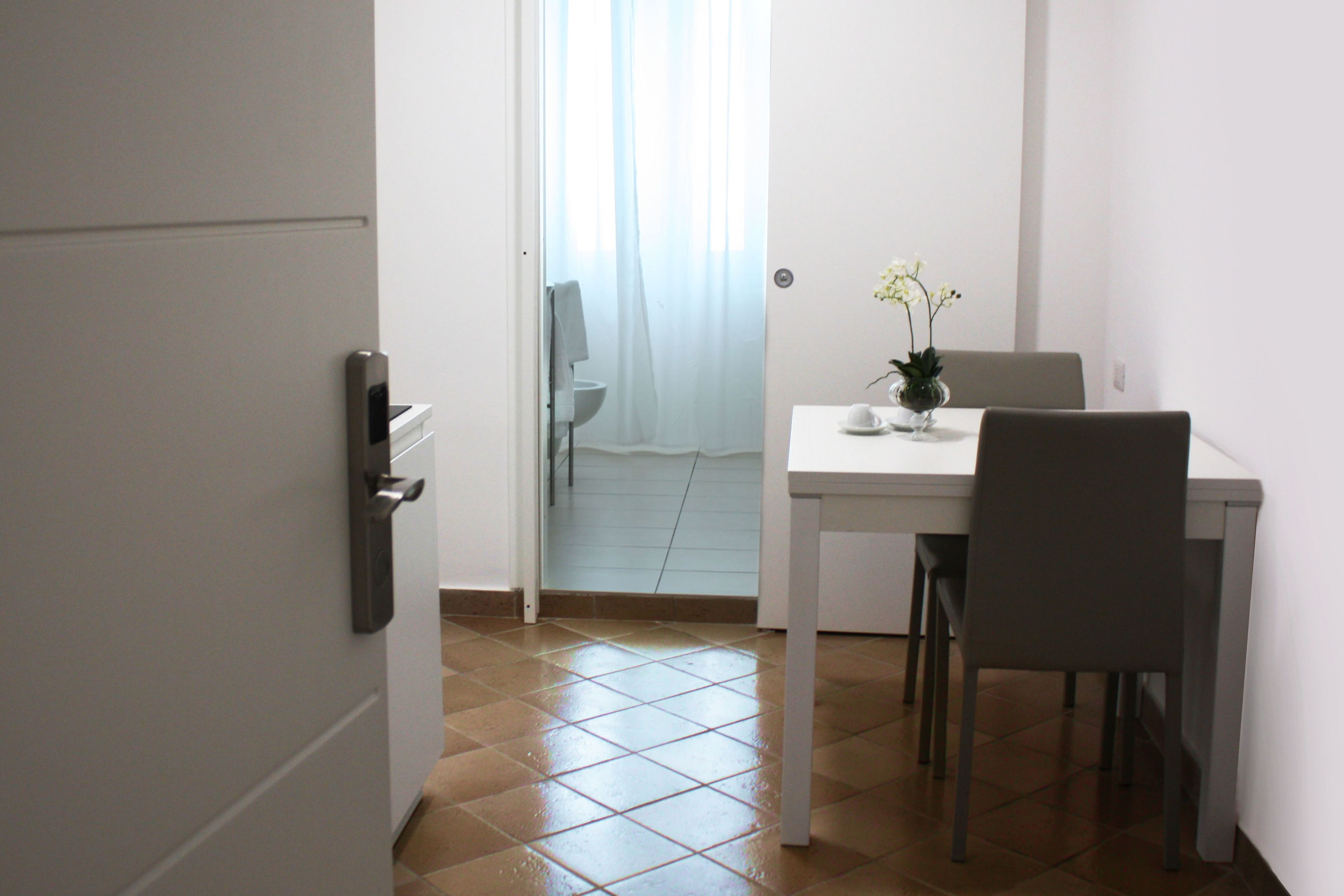A small, clean room with a white door, a white table, a chair, and a small potted plant.