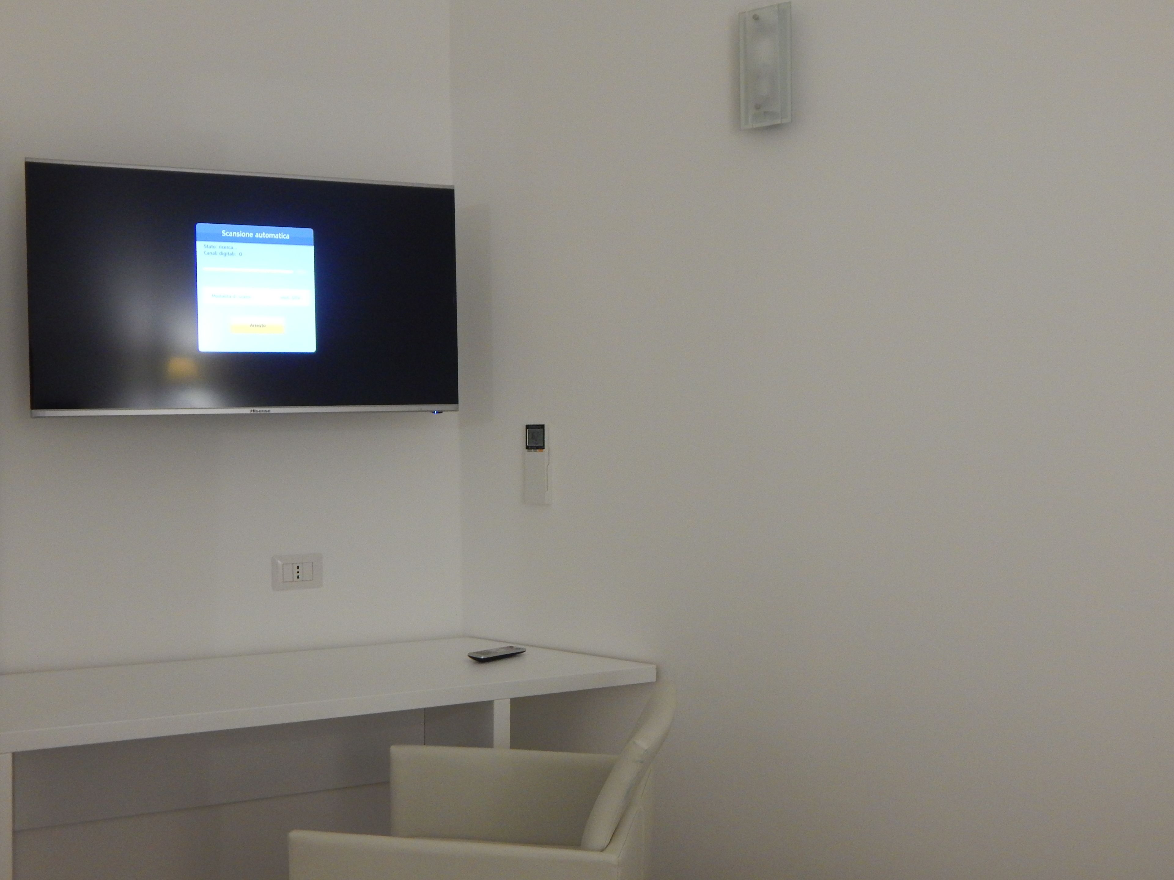 A modern room with a flat-screen TV mounted on the wall, a white desk, and a white chair.
