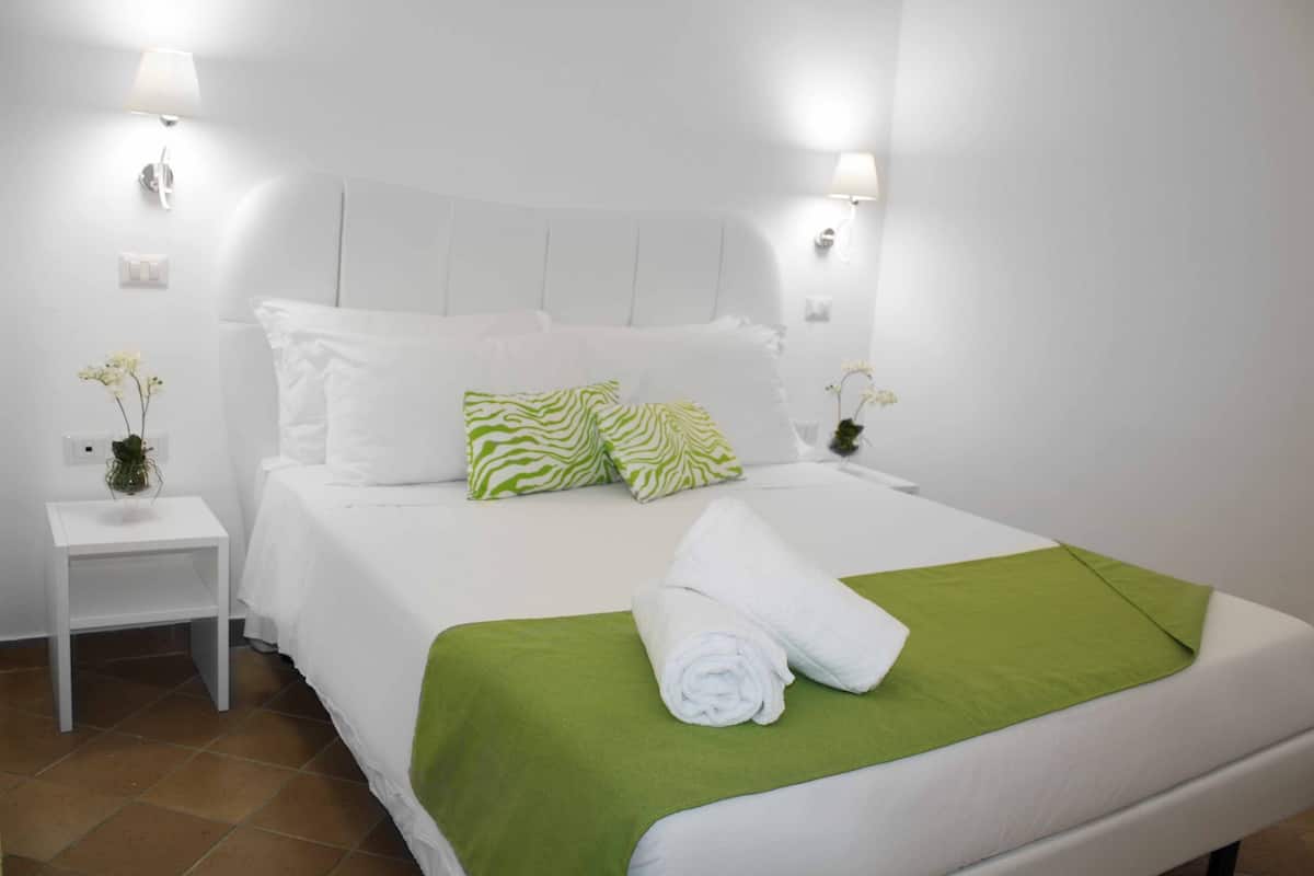 Ein ordentlich bezogenes Bett mit weißer und grüner Bettwäsche, einer grünen Tagesdecke und einem gerollten Handtuch an der Seite.