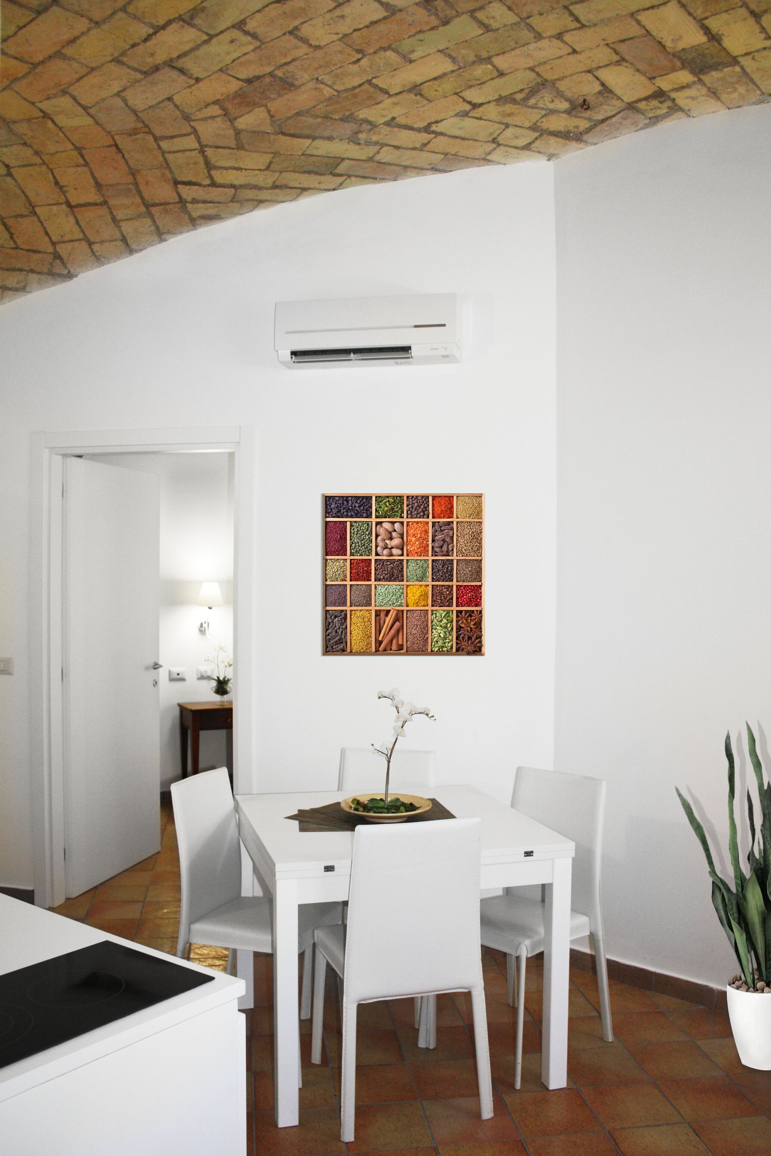 A dining area with a white table and chairs, a potted plant, and a colorful tile artwork on the wall.