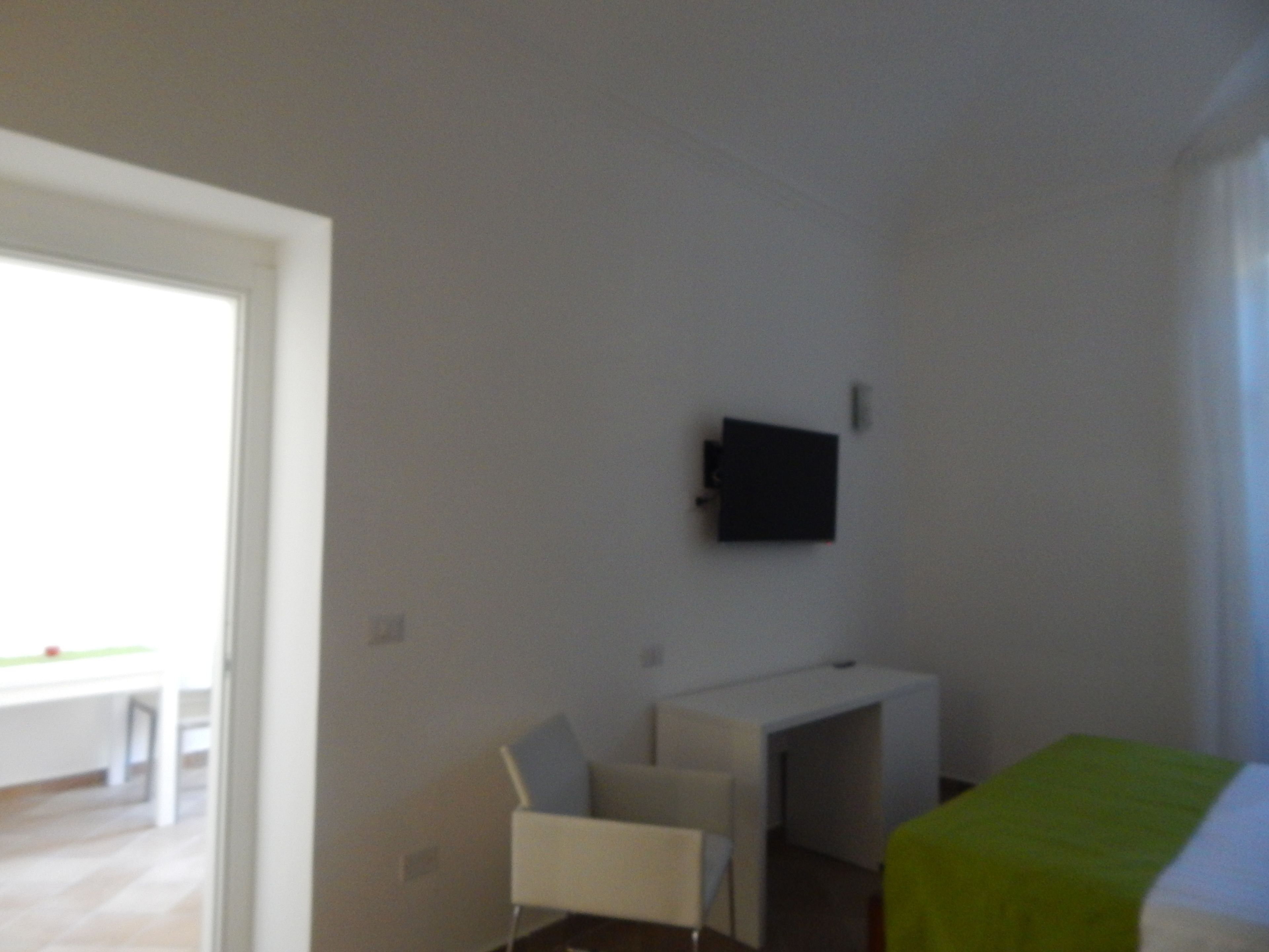 Una habitación pequeña y escasamente amoblada, con cama, escritorio y silla.