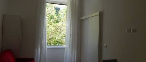 A room with a large window, a red sofa, a small table with a cup, and a white cabinet.