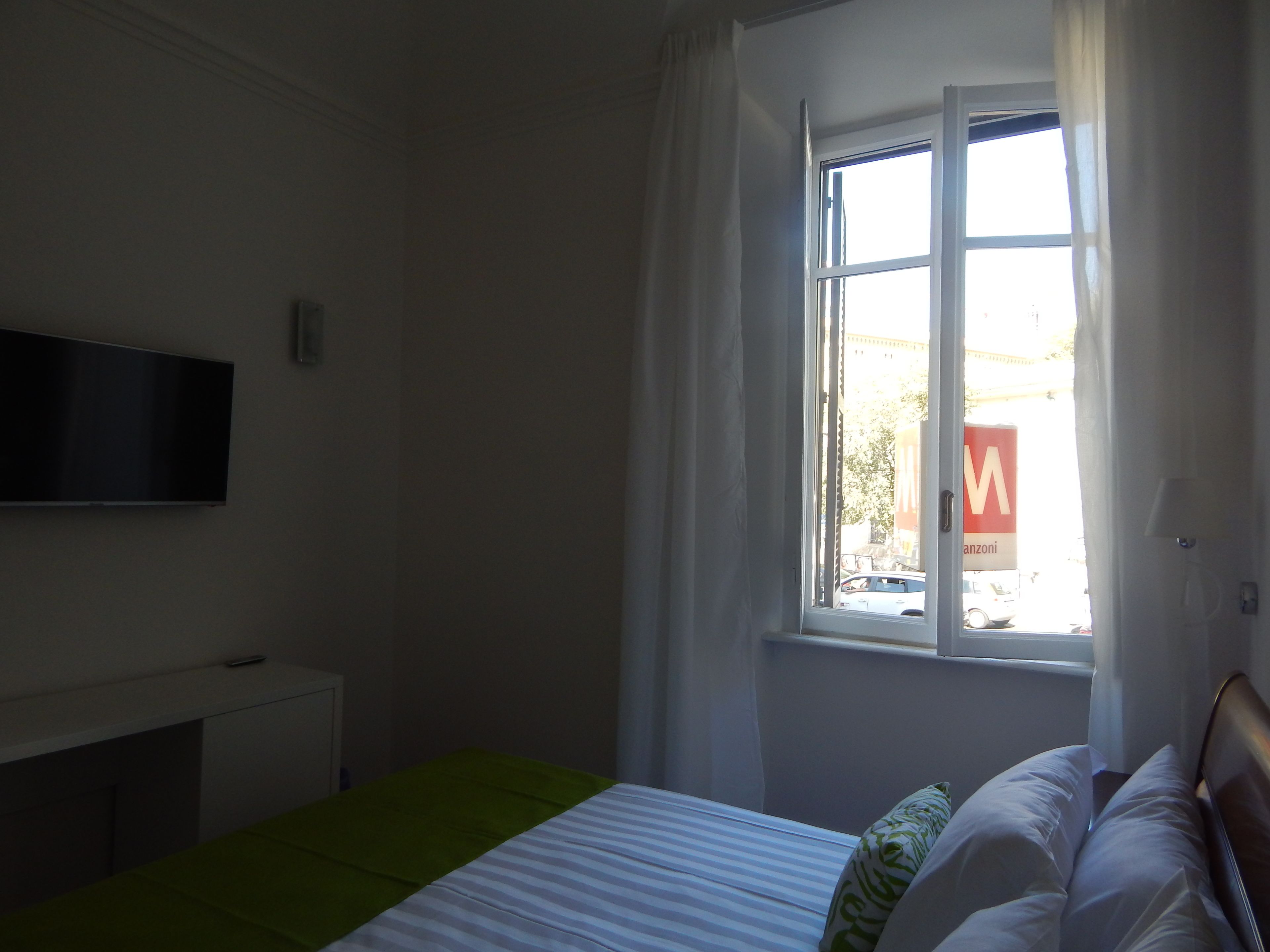 Un dormitorio con cama, televisión de pantalla plana en la pared, ventana con cortinas y vistas al exterior.