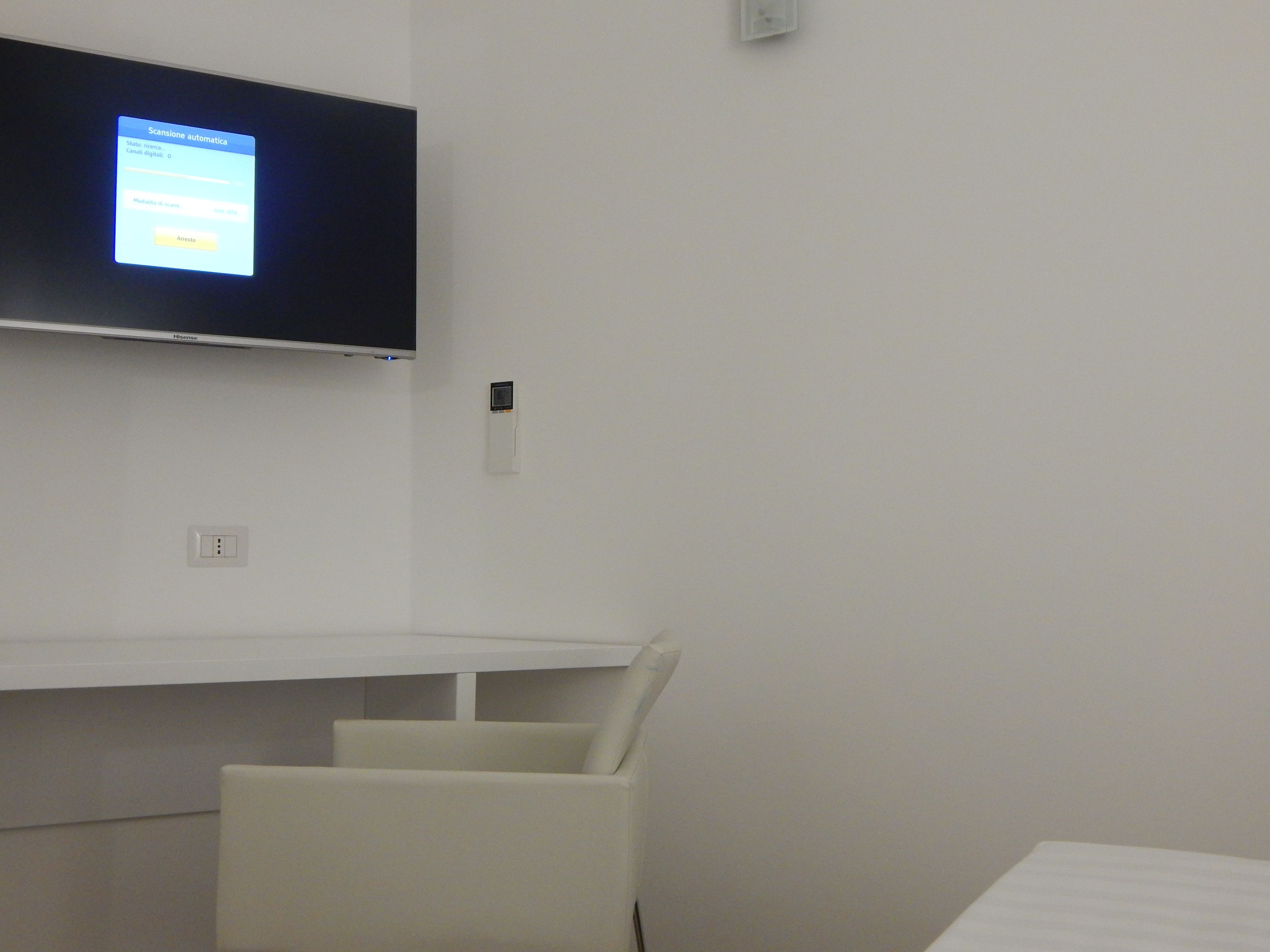 A room with a flat-screen TV mounted on the wall, a white desk, and a white chair.