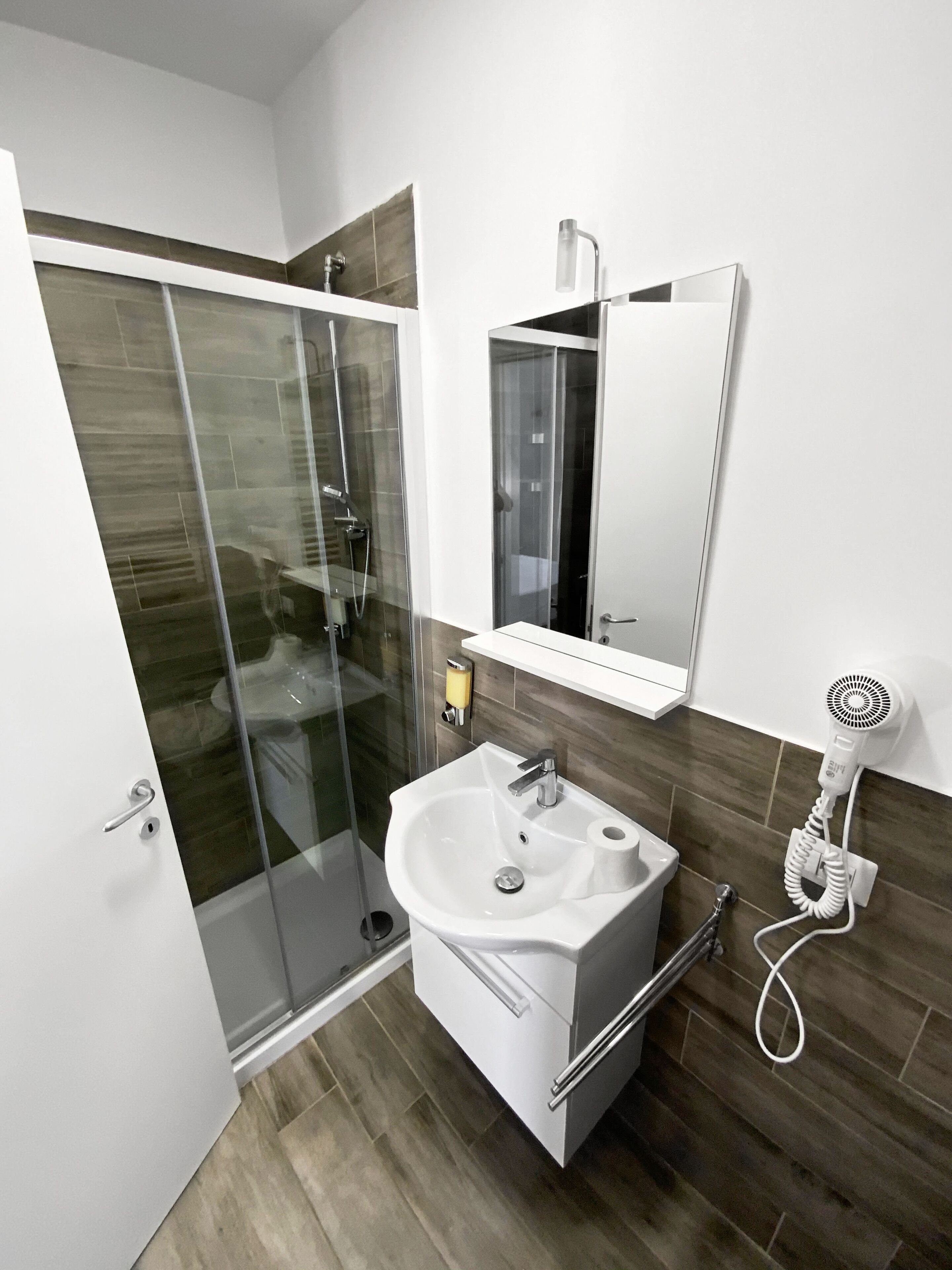 A modern bathroom with a glass-enclosed shower, a white sink with a mirror above it, and a hairdryer on the wall.