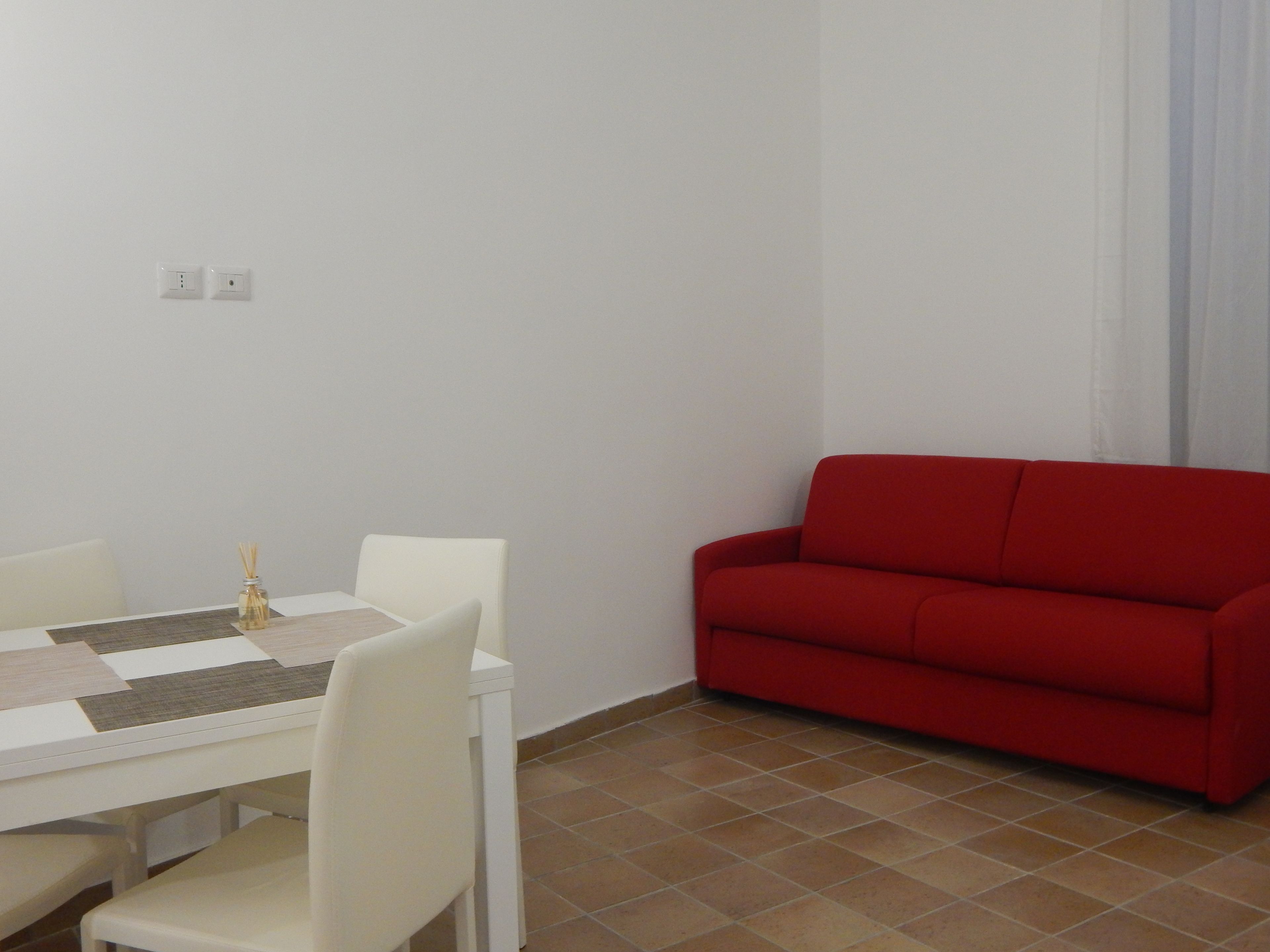 A dining area with a white table and chairs, a red sofa, and a tiled floor.