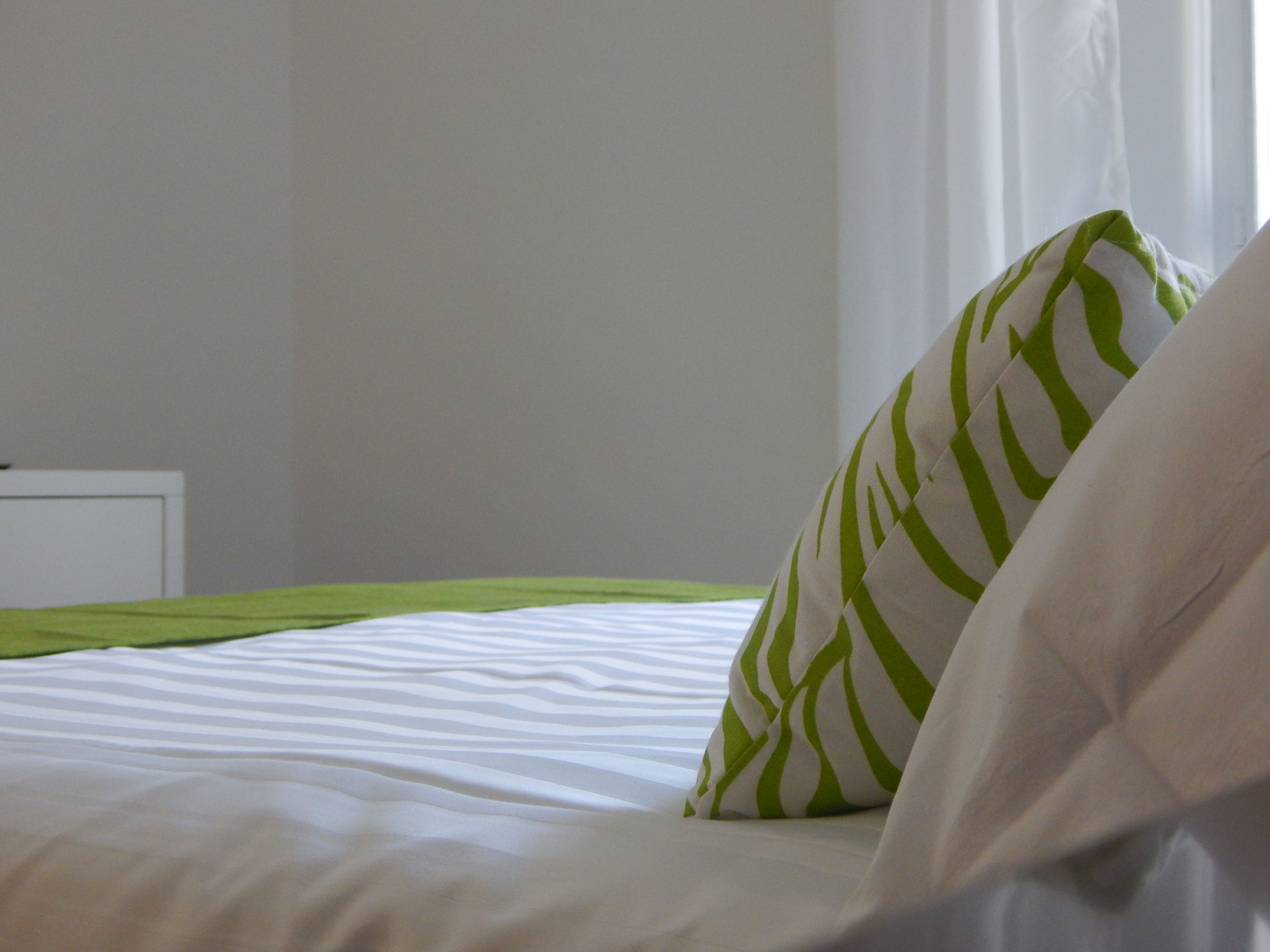 A neatly made bed with white bedding and a green and white striped pillow.
