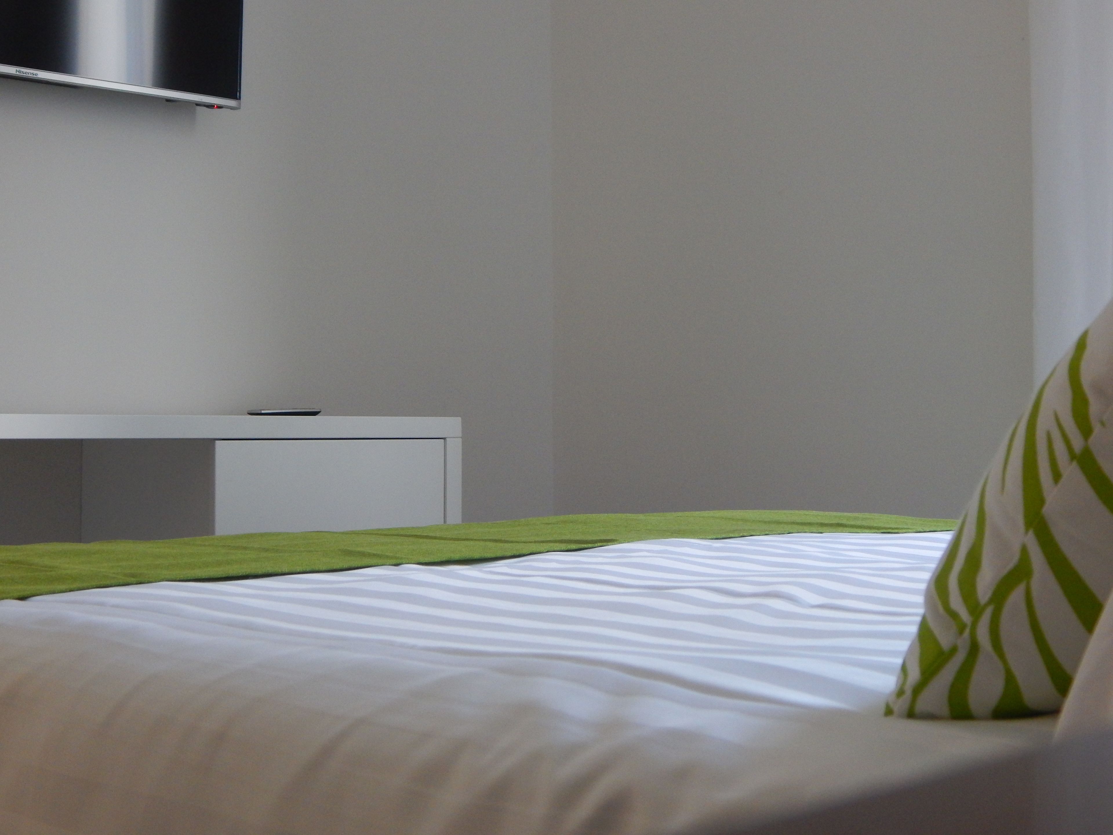 Une chambre d’hôtel moderne équipée d’un lit, d’une table de chevet et d’un téléviseur à écran plat fixé au mur.