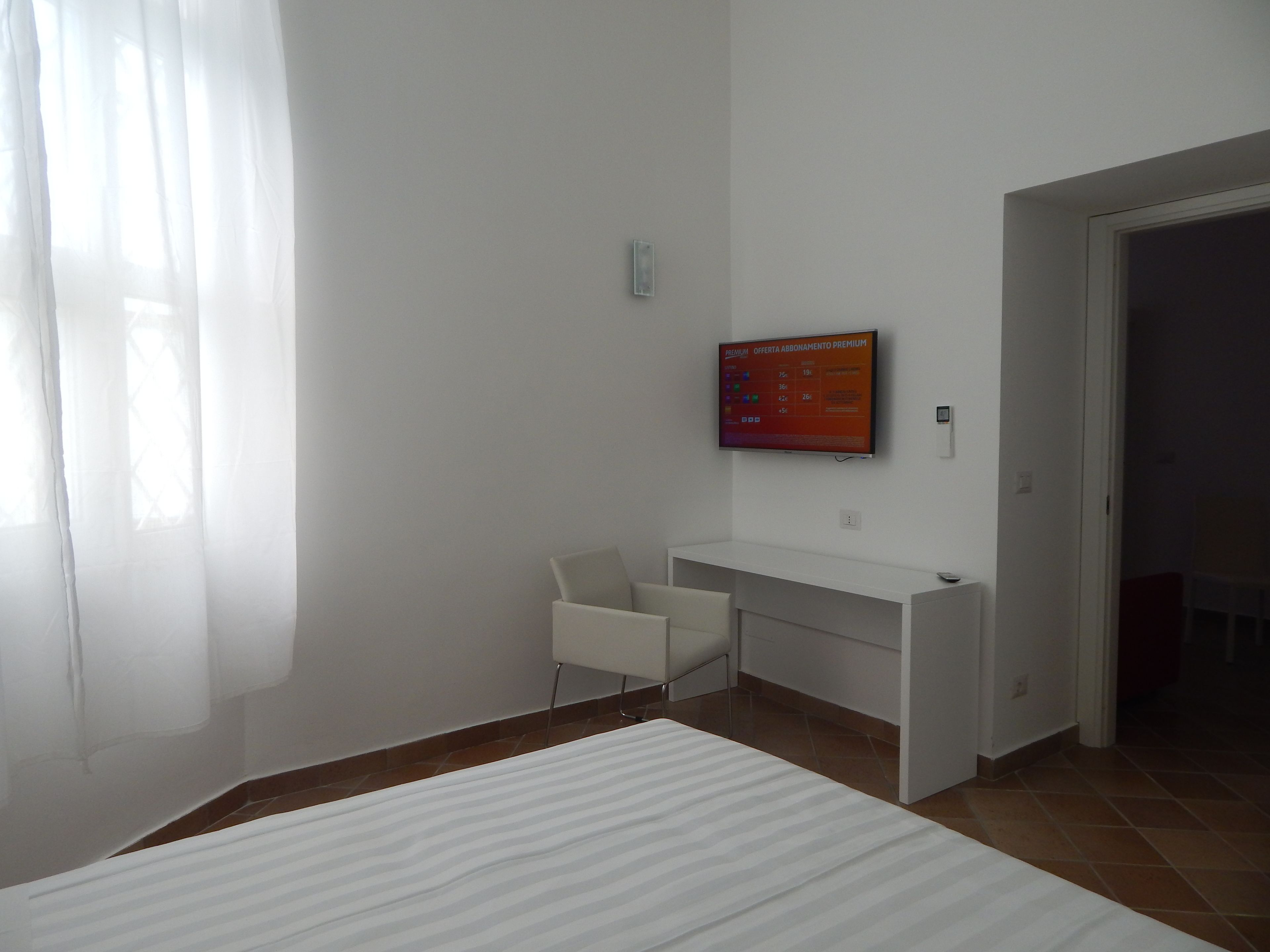 A hotel room with a bed, a desk, and a TV mounted on the wall.