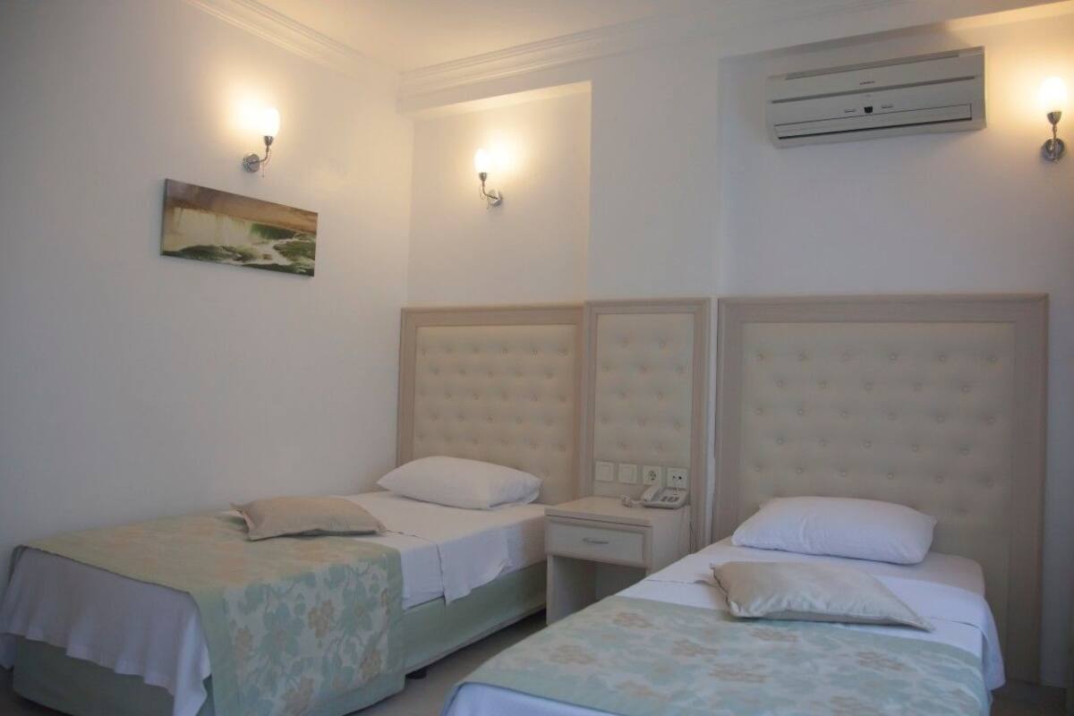 Una habitación con dos camas, cada una con cabecera y mesitas de noche. Hay un aire acondicionado de pared y dos lámparas de pared.