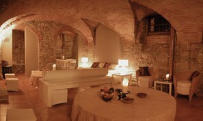 A cozy room with stone walls, a round table with candles, and a white sofa. - Villa Scati Apartments (Melazzo)