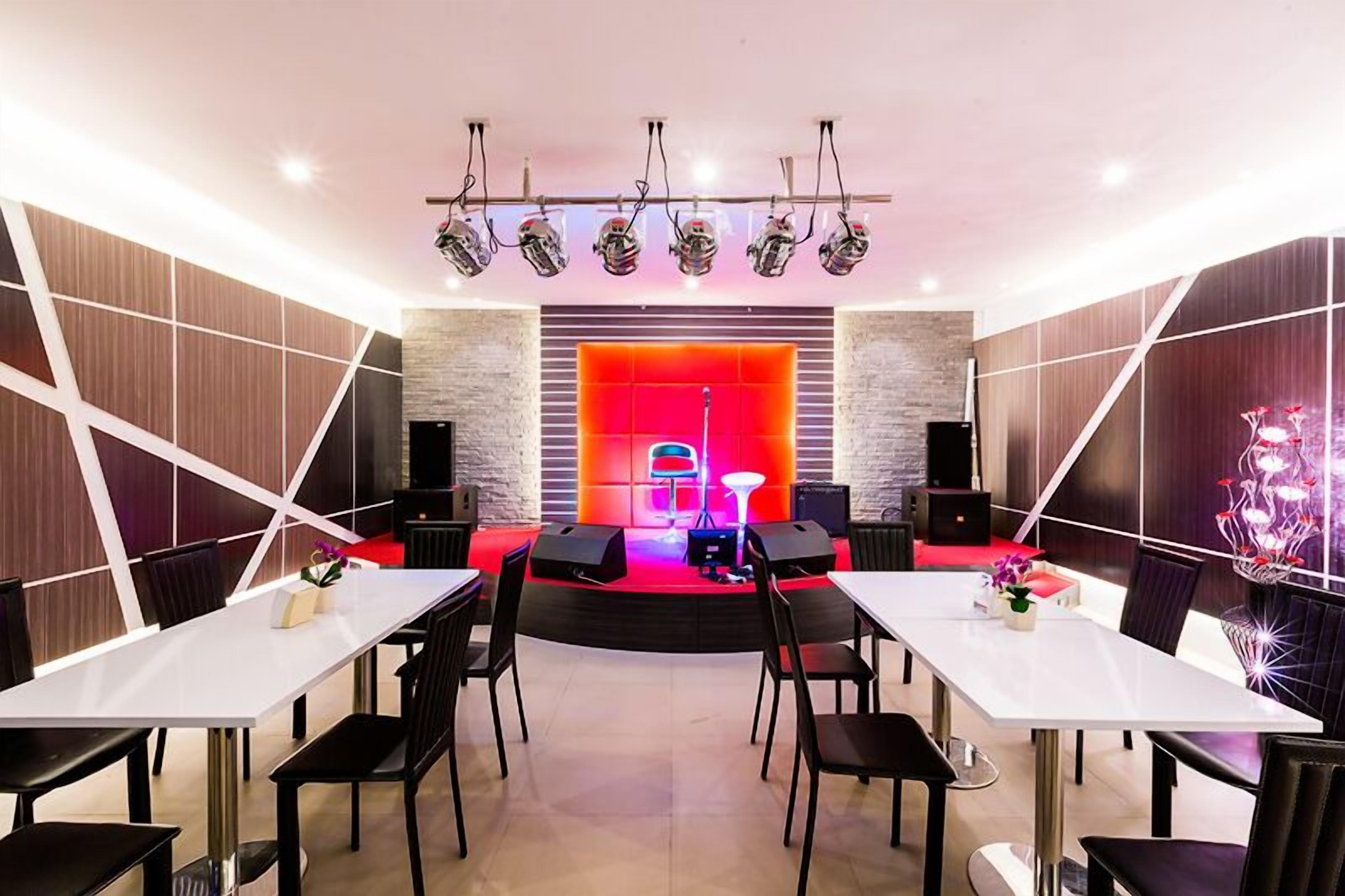 Une salle de conférence moderne, dotée d’une scène, de tables blanches et de chaises noires.