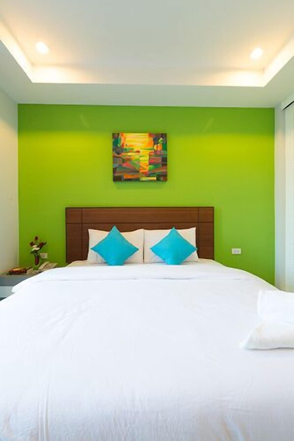 Un dormitorio con cama, paredes verdes, una lámpara de techo y un cuadro en la pared.