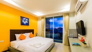 Une chambre d’hôtel avec un lit, un bureau avec une télévision, une fenêtre avec des rideaux et un tableau au mur.