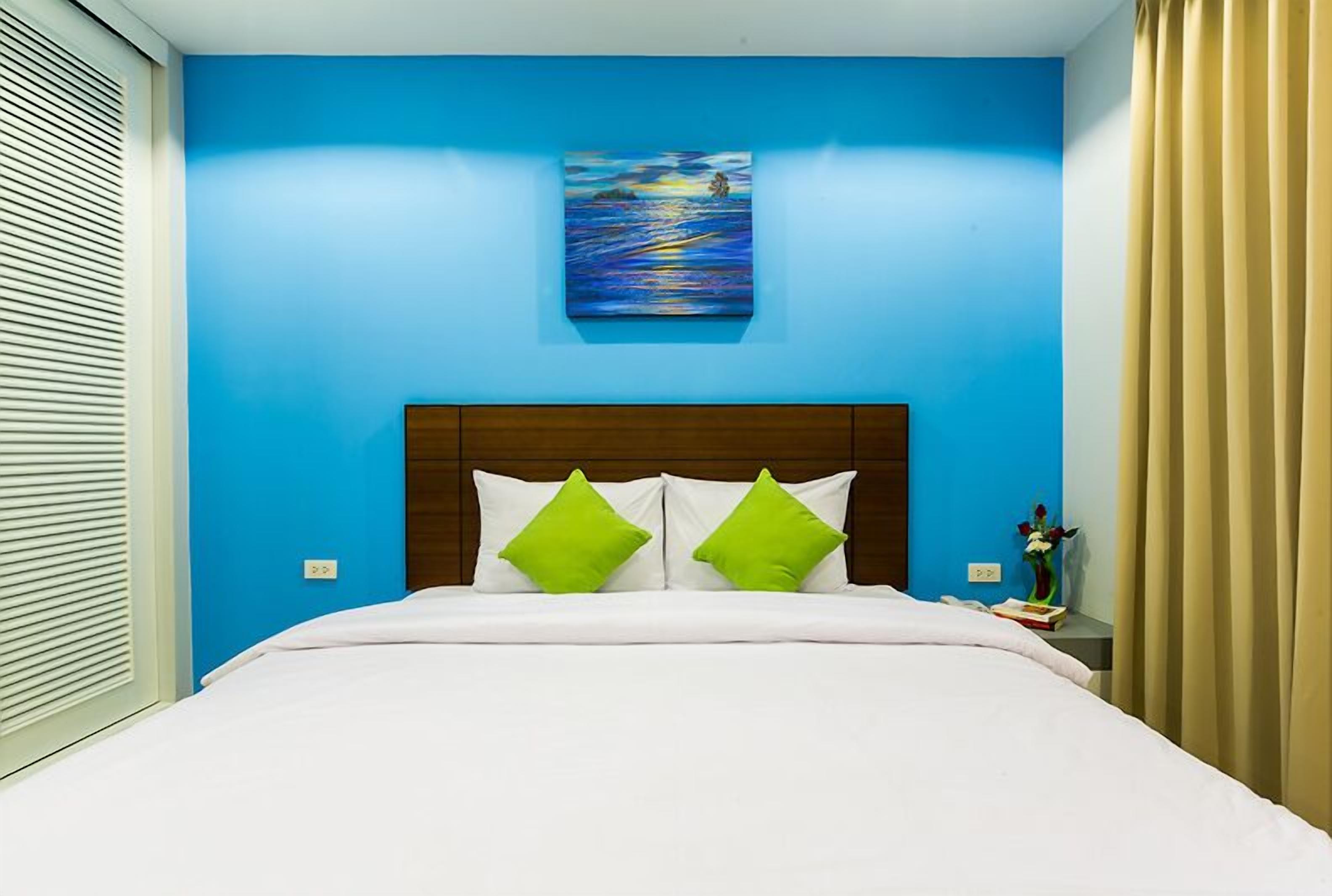 A hotel room with a blue wall, a painting above the bed, and a wooden headboard.