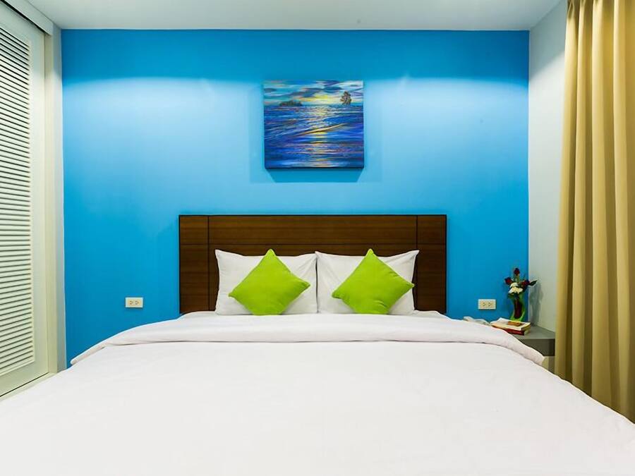 A hotel room with a blue wall, a painting above the bed, and a wooden headboard.