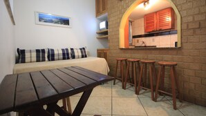A cozy room with a wooden table, a sofa with striped cushions, and a kitchen area with wooden cabinets and stools. - Copacabana 705 B (Rio de Janeiro)