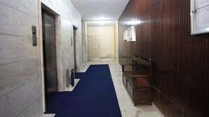 A hallway with a blue carpet, an elevator, a wooden panel wall, and a door leading to a room. - Copacabana 705 B (Rio de Janeiro)