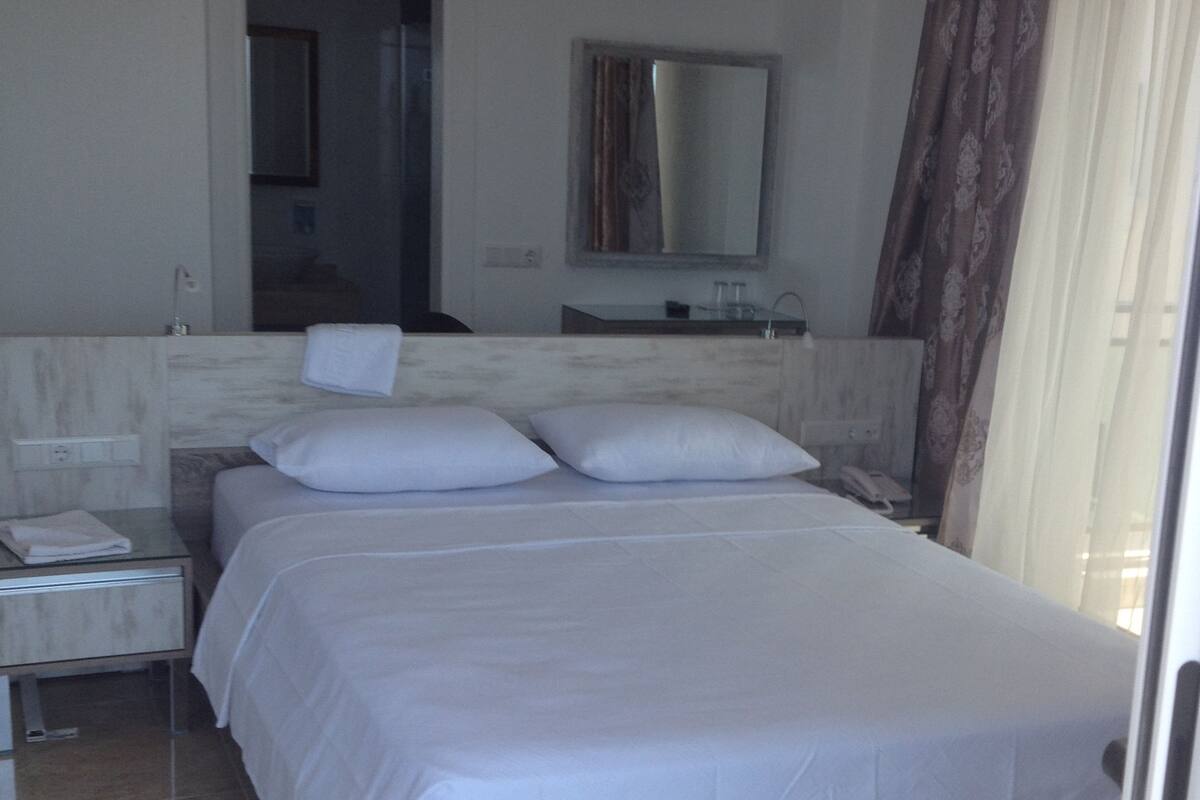 Un dormitorio moderno con una cama grande, una mesita de noche, un espejo y un baño visible a través de una puerta abierta.