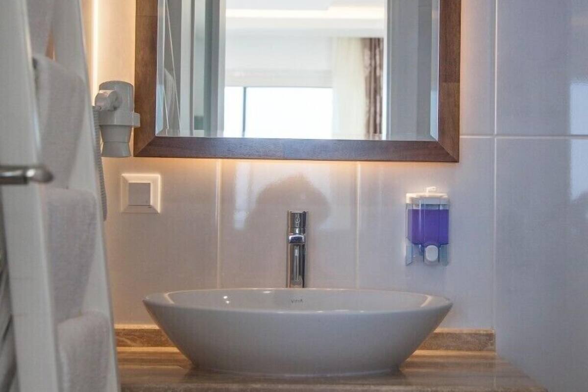 Un baño con un lavamanos blanco tipo recipiente, una encimera de madera, un espejo con marco de madera y un dispensador de jabón.