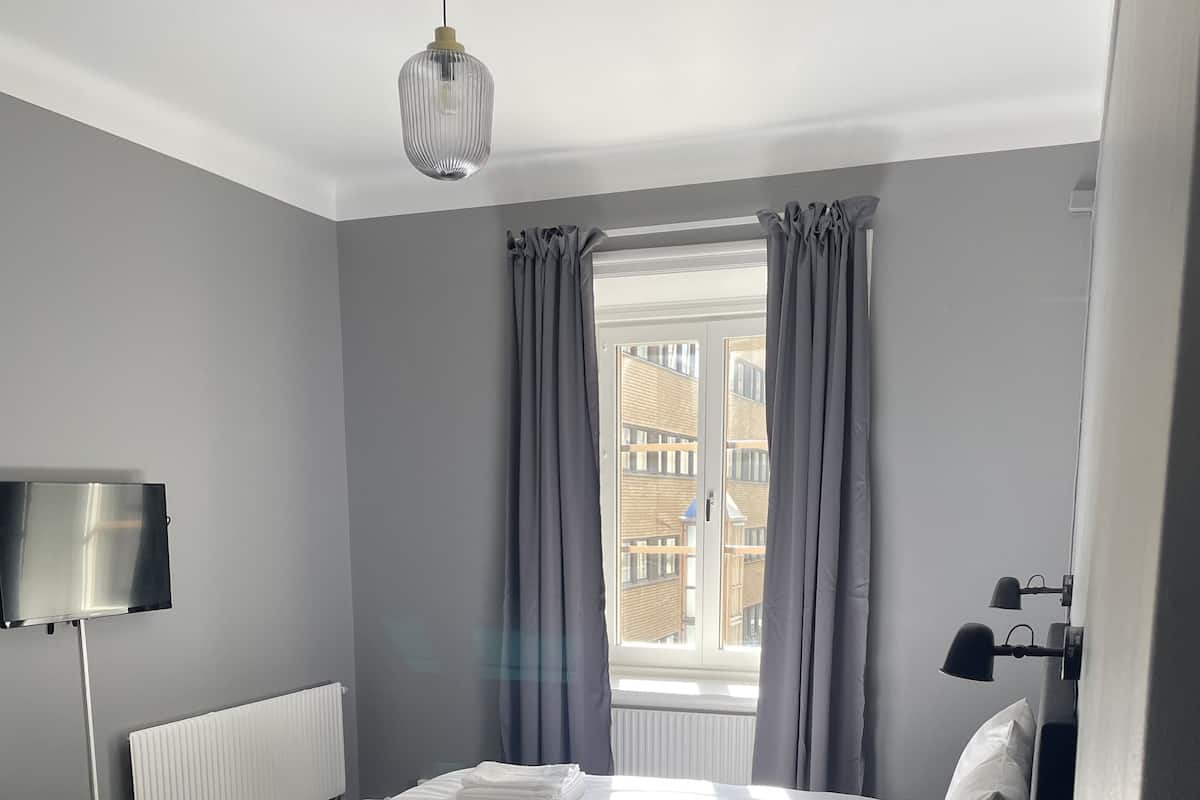 A modern hotel room with a large bed, a flat-screen TV, a radiator, and a window with curtains.
