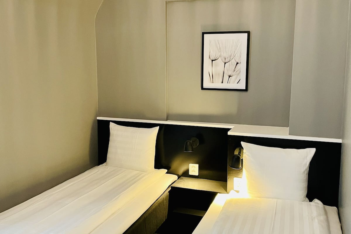 A hotel room with two single beds, a framed picture on the wall, and a bedside table with a lamp.