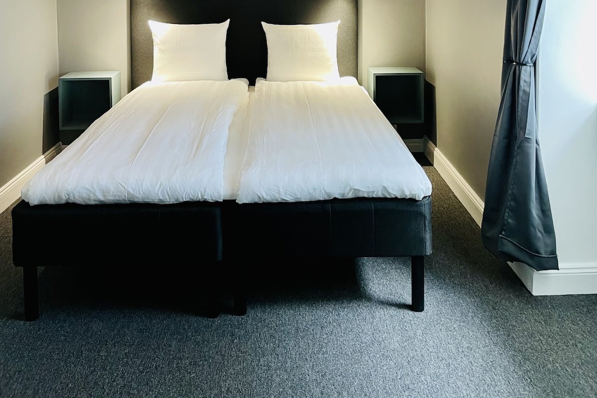 A bedroom with a large bed, two bedside tables, a ceiling light, a framed picture on the wall, and a window with curtains.