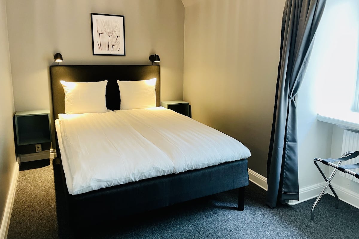A neatly made bed in a hotel room with a headboard, bedside tables, and a framed picture on the wall.