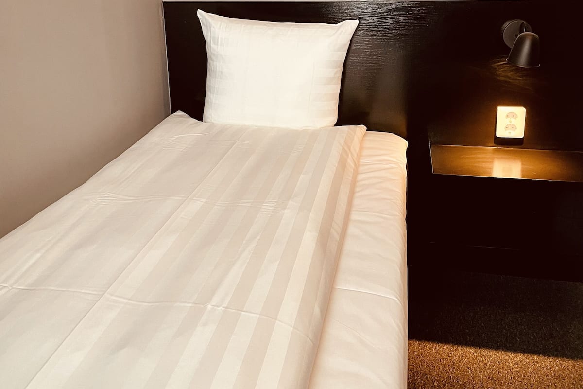 A neatly made bed with a white comforter and a pillow, a framed artwork above the bed, and a bedside table with a lamp.
