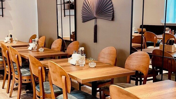 A restaurant with wooden tables and chairs, a decorative fan, and pendant lighting. - Birka Hotel (Stockholm)