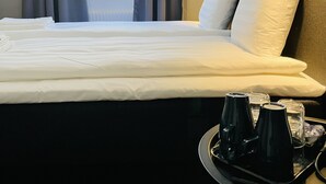 A hotel room with a neatly made bed, a bedside lamp, a tray with a coffee maker, and a view of the outside through a window with curtains. - Birka Hotel (Stockholm)