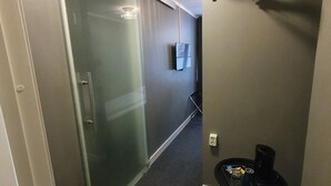 A hallway with a glass partition, a small table with a coffee maker, and a wall-mounted TV. - Birka Hotel (Stockholm)