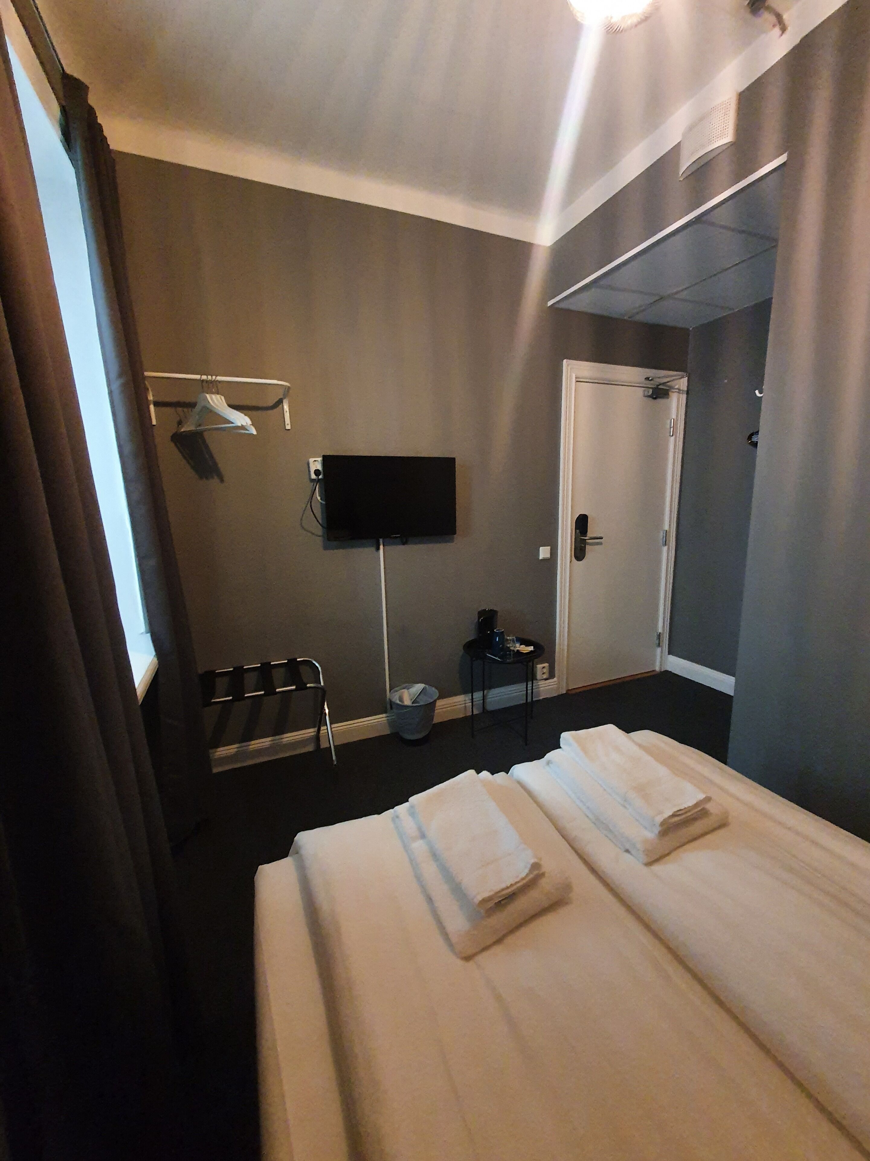 Quarto de hotel com cama, televisão, cadeira, mesinha e porta.