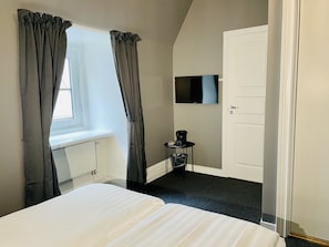 A bedroom with a bed, a window with curtains, a radiator, a television, and a door.