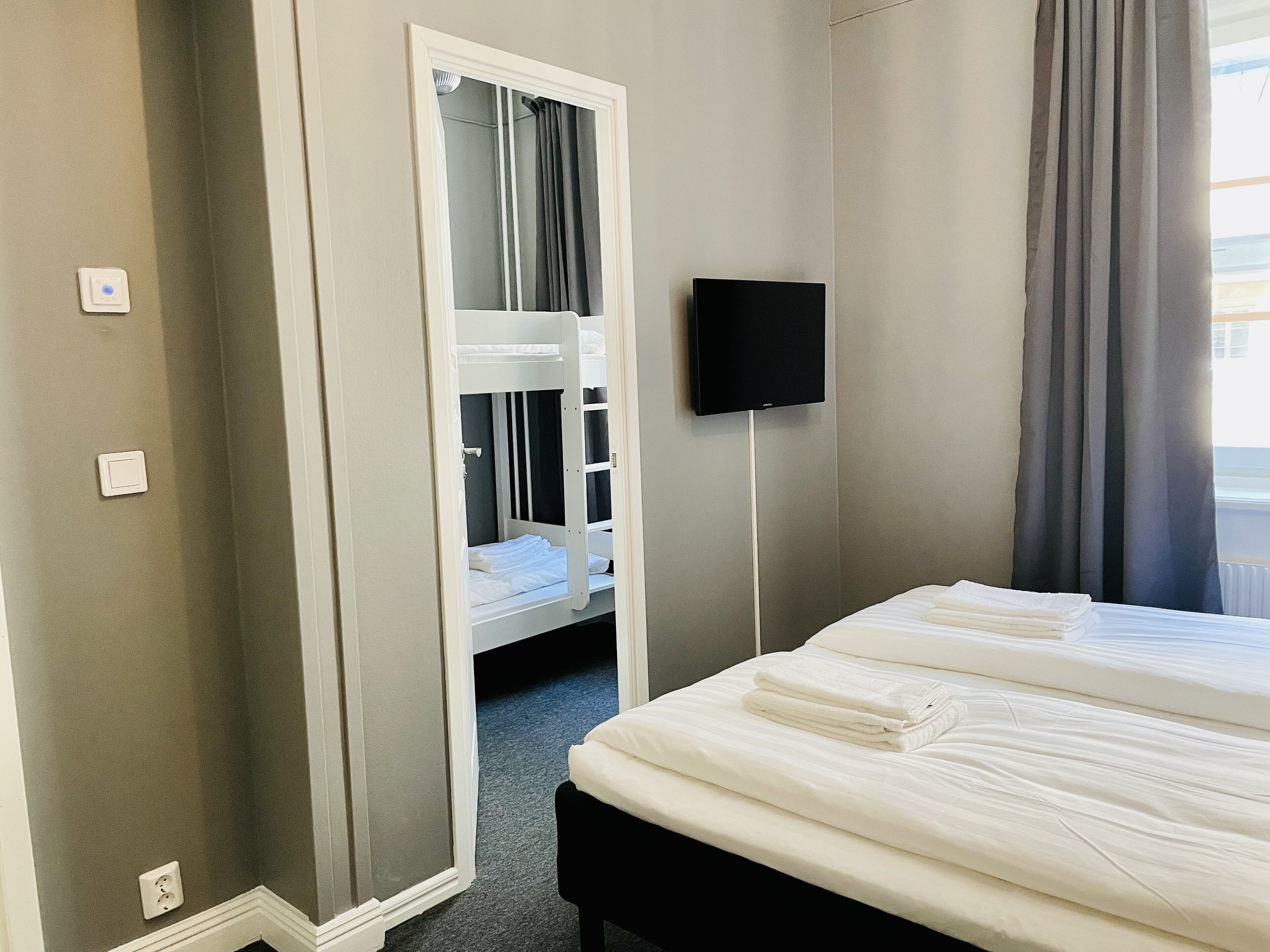 A hotel room with a bunk bed, a flat-screen TV, and a large window with curtains.