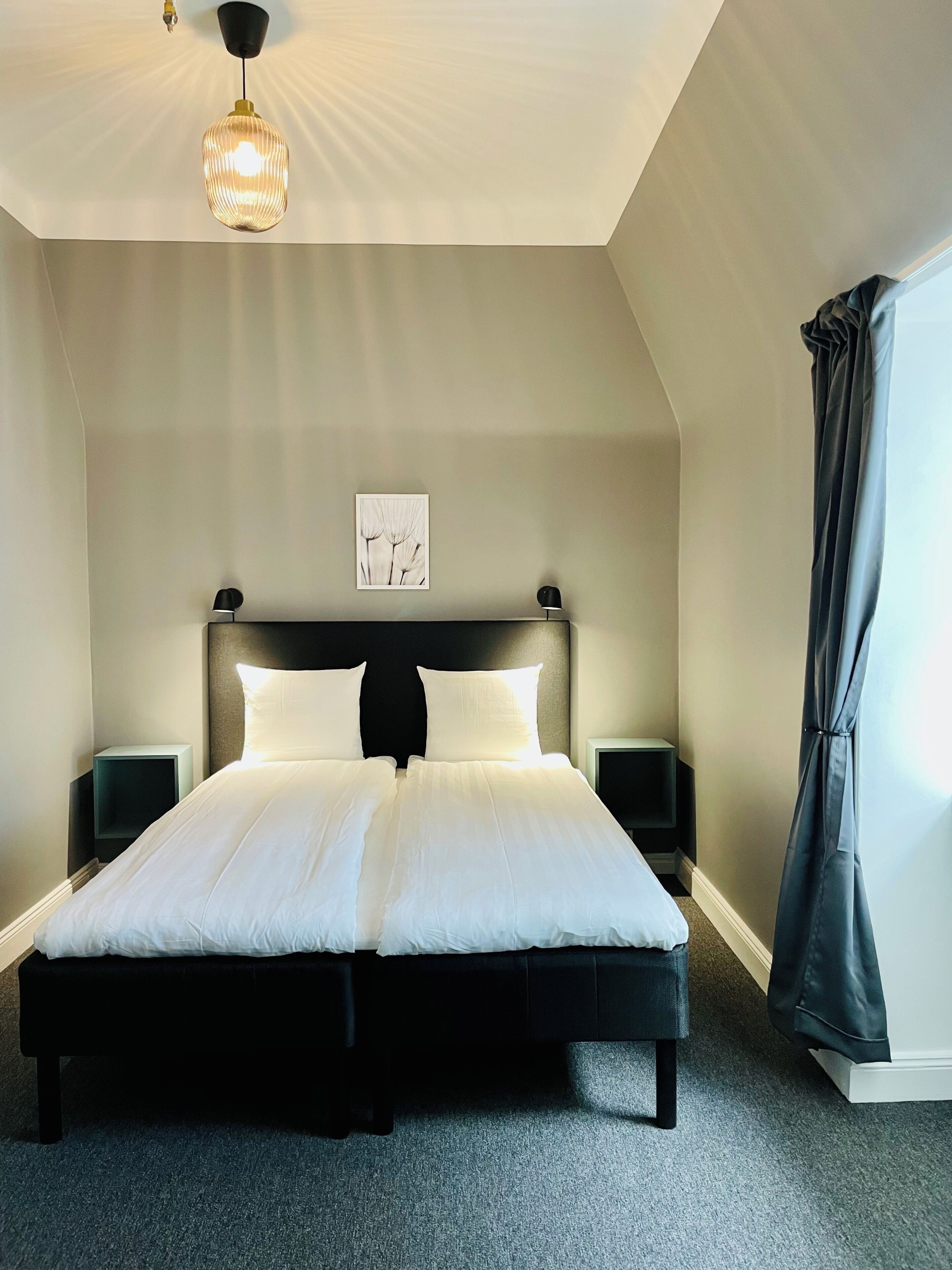 A neatly arranged bedroom with a large bed, two bedside tables, a ceiling light, and a framed picture on the wall.