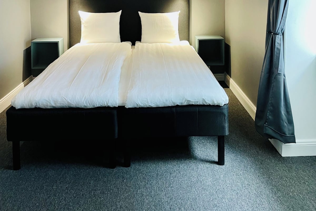 A bedroom with a large bed, two bedside tables, a ceiling light, a framed picture on the wall, and a window with curtains.
