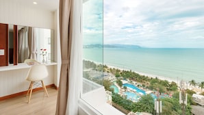 A modern hotel room with a large window overlooking a beach and a pool area.