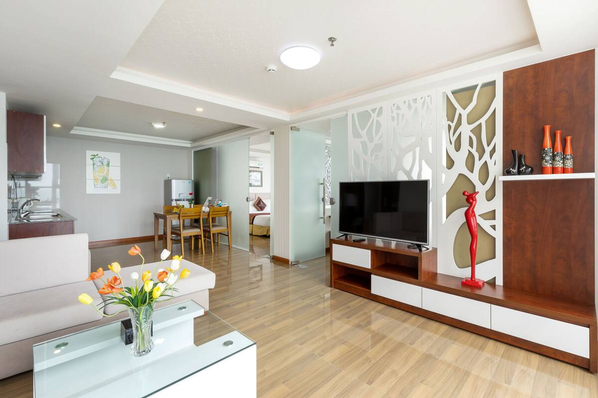 A modern living room with a flat-screen TV, a glass coffee table, and a vase of flowers.