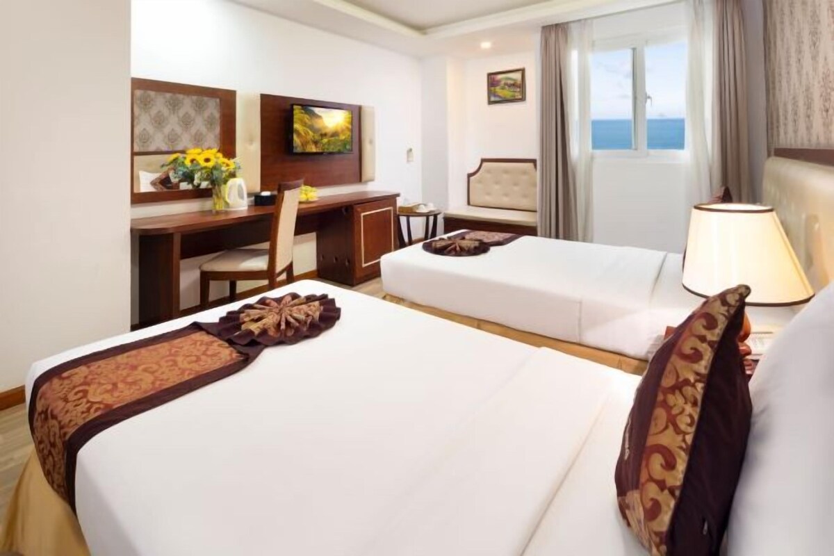 Habitación de hotel con dos camas, un escritorio, televisor y ventana con vistas.